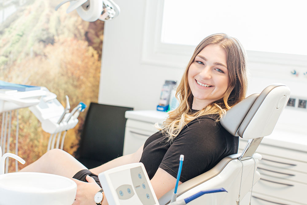 Zahnarzt Köln Innenstadt - Dr. Bongartz - junge Frau sitzt lächelnd auf Zahnarztstuhl